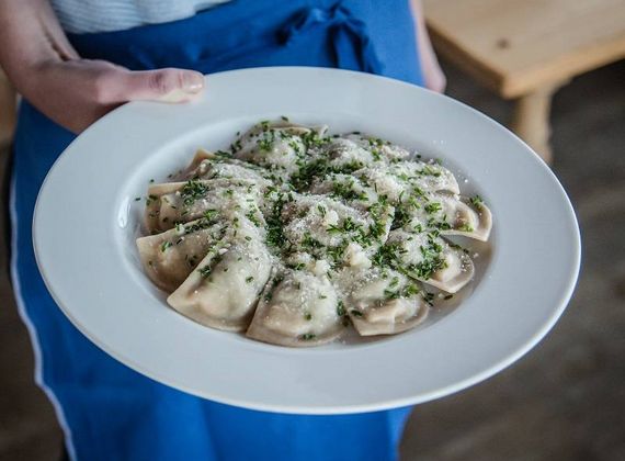 Una persona con grembiule blu tiene un piatto bianco di pasta con erbe e formaggio grattugiato.