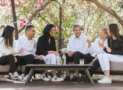 Die Familie Ladurner sitzt im Gartensitzbereich unter blühenden Bäumen und spricht miteinander.
