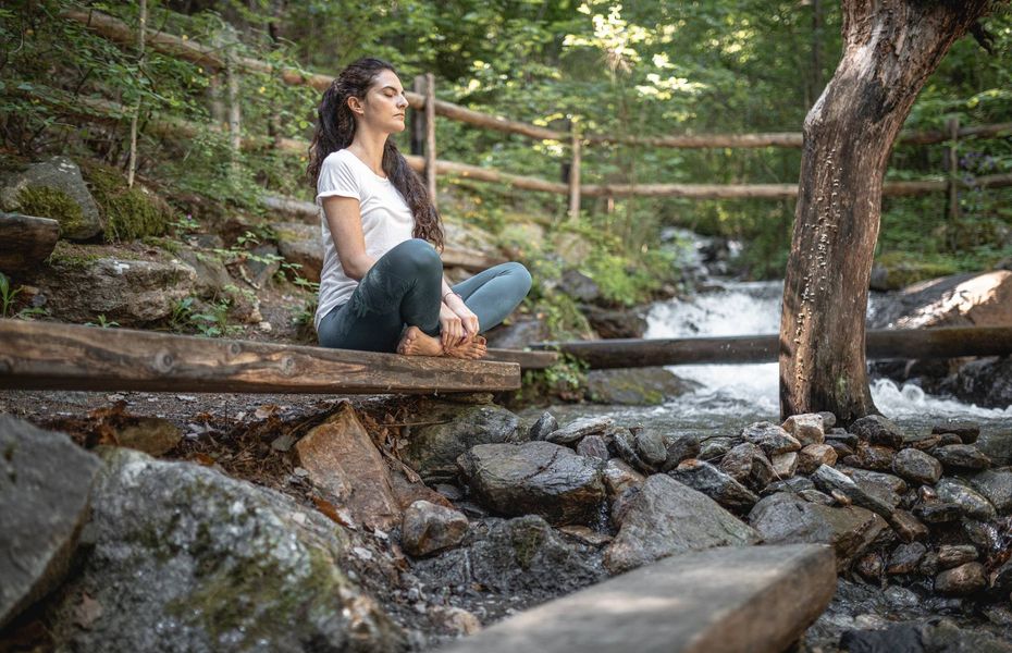 Wellnessruheraum im Grünen in Naturns Eine Frau sitzt barfuß auf einer Holzplattform am Bach und entspannt sich im Grünen.