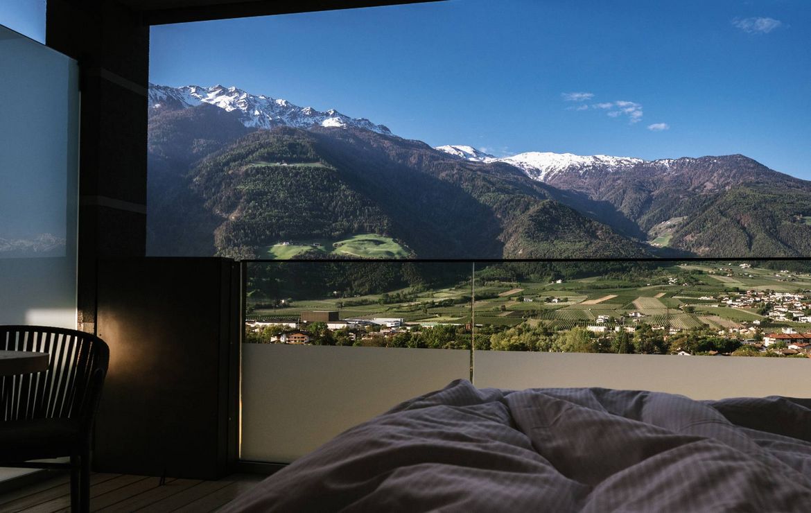 Un letto è rivolto verso una grande finestra con vista su montagne e valle.