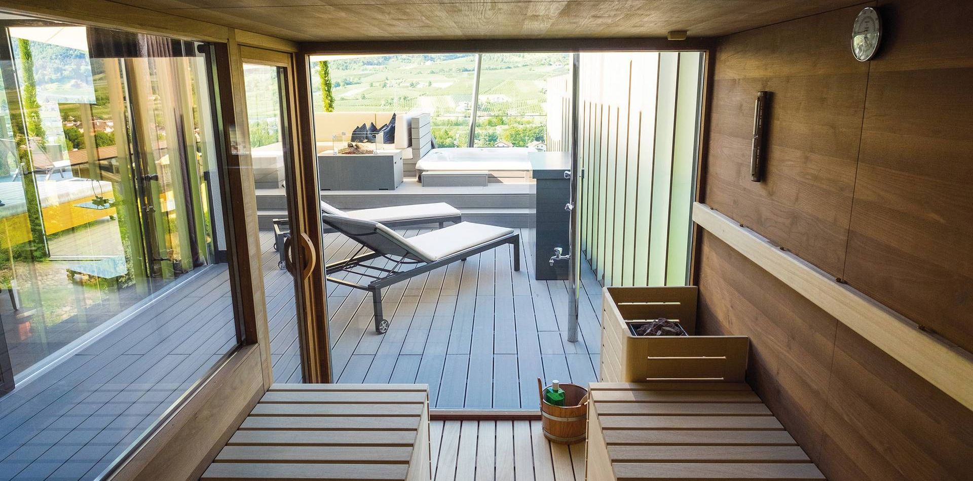 Una sauna privata si apre su una terrazza in legno con lettini e vista esterna.
