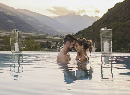 Ein Paar steht im Infinity-Pool und berührt sich vor Bergkulisse im Abendlicht.