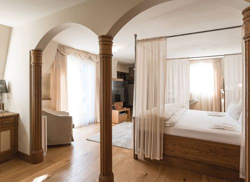 Eine helle Luxussuite mit Himmelbett, Holzboden, Vorhängen und Sitzbereich im Preidlhof.