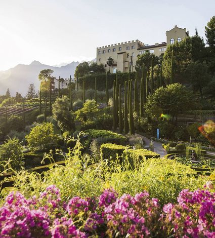 Der mediterrane Garten mit Zypressen und Blick auf das Hotel liegt in der Abendsonne.