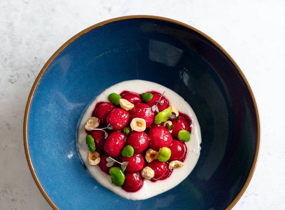 A blue bowl holds a plated gourmet dessert topped with berries, green garnish and nuts on a white cream base.