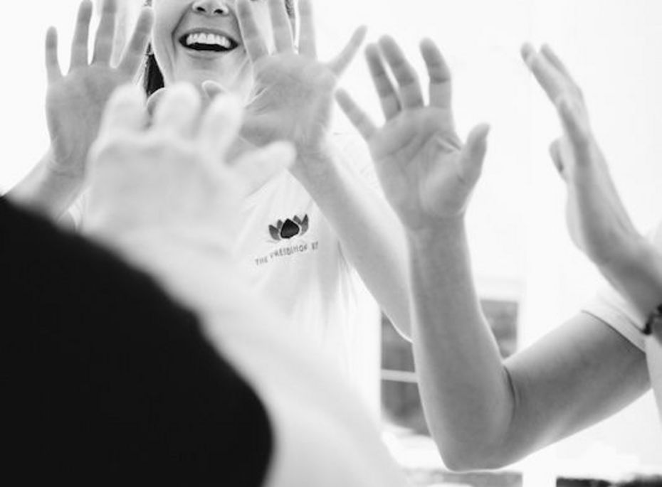 Spa-Behandlung mit Team im Preidlhof Eine lächelnde Mitarbeiterin führt eine Spa-Behandlung an einer Person durch, während mehrere Hände im hellen Raum zu sehen sind.