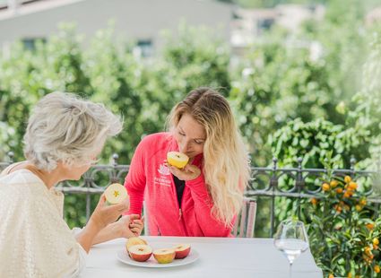 Eine ältere Frau und eine junge Frau essen an einem Tisch auf der Terrasse Obst.