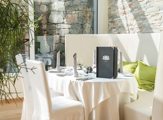 A set dining table with white tablecloths and folded napkins stands beside a cushioned booth in a gourmet restaurant.