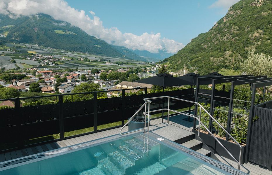 Ein kleiner Infinity-Pool mit Treppe und Geländer liegt auf einer Terrasse mit Blick ins Tal und auf die Berge.