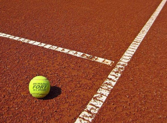 Ein Tennisball liegt auf dem roten Sandplatz neben der weißen Linienmarkierung.