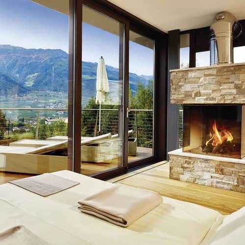 Ein helles Wellnesszimmer mit Kamin, großen Glasfronten und Blick auf die Berge und das Tal.