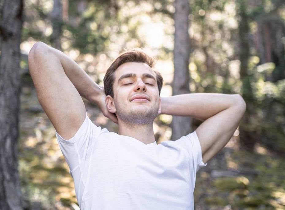 Wanderer entspannt im Wald am Preidlhof Ein Mann in weißem T-Shirt entspannt mit verschränkten Armen im Wald und genießt die Sonne.