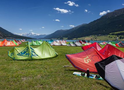 Bunte Kitesurf-Schirme liegen auf einer Wiese vor den Bergen im Tal bei Naturns.