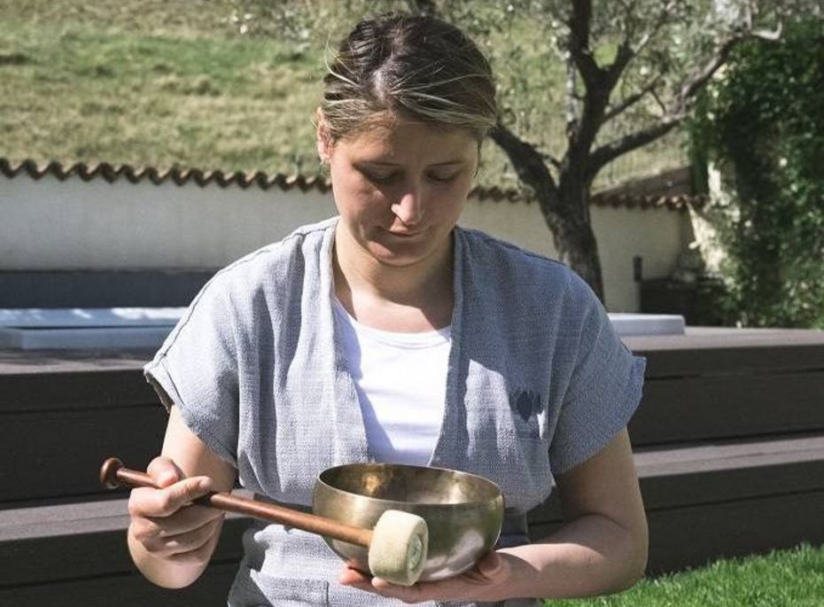 Klangschalenmassage im Wellnesshotel in Naturns Eine Frau sitzt im Garten und hält eine Klangschale mit Schlegel in den Händen.