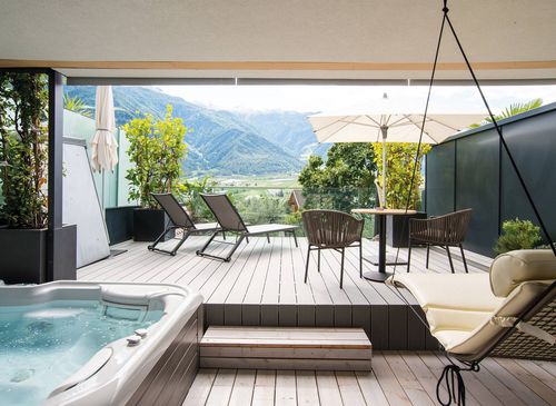 Eine private Terrasse der Suite Romantic Garden mit Whirlpool, Liegen, Tischgruppe und Bergblick.