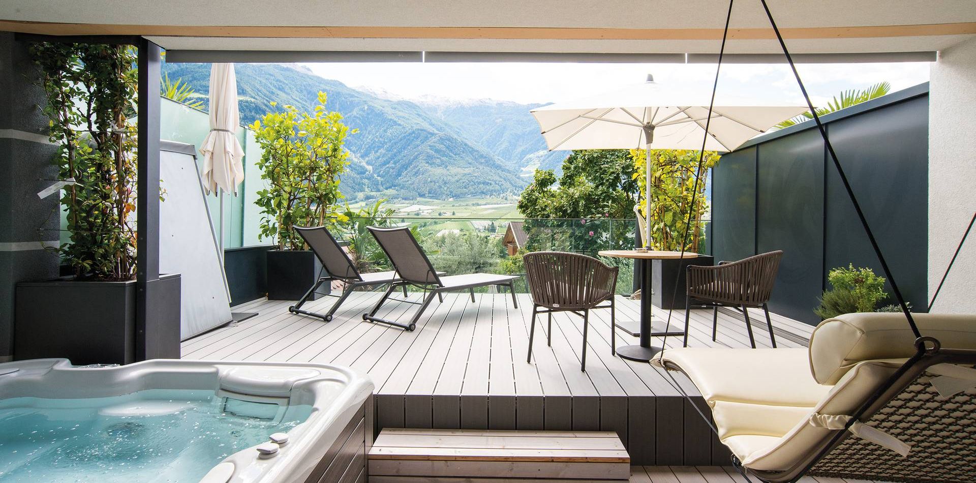 Eine private Terrasse der Suite Romantic Garden mit Whirlpool, Liegen, Tischgruppe und Bergblick.