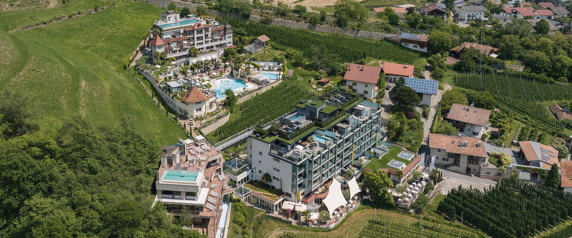 Luftaufnahme einer Hotelanlage mit Pool, Terrassen und umliegenden Weinbergen am Rand von Naturns.