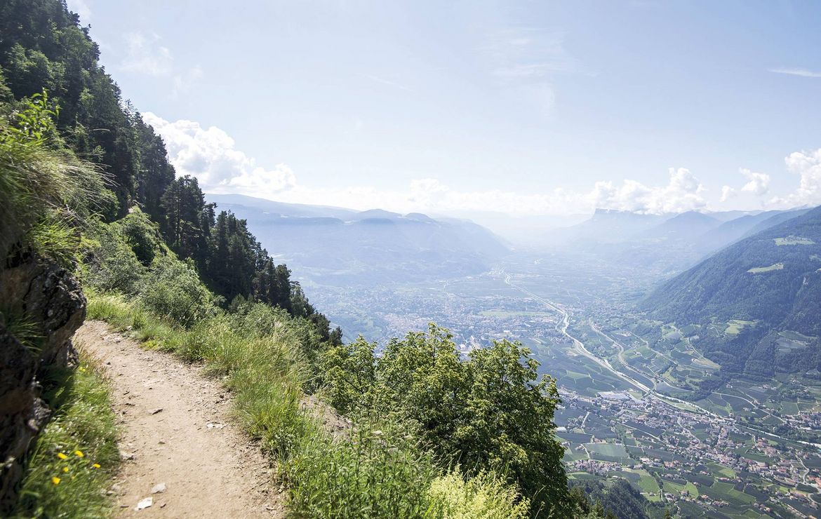 Ein schmaler Wanderweg verläuft am Hang mit Blick über das Tal und die Berge im Naturpark Texelgruppe.