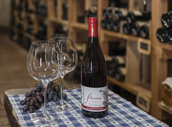 Due calici, una bottiglia di vino rosso e un grappolo d'uva sono su un tavolo a quadri in cantina.