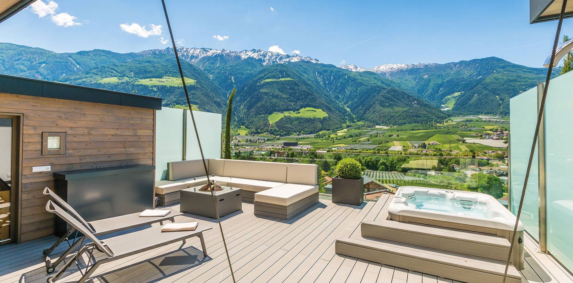 A penthouse suite terrace with lounge seating, a sun lounger and a whirlpool overlooking the mountains.