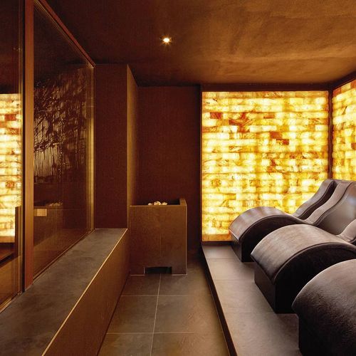 Eine warme Spa-Lounge mit gepolsterten Liegen und goldfarben beleuchteten Wänden.