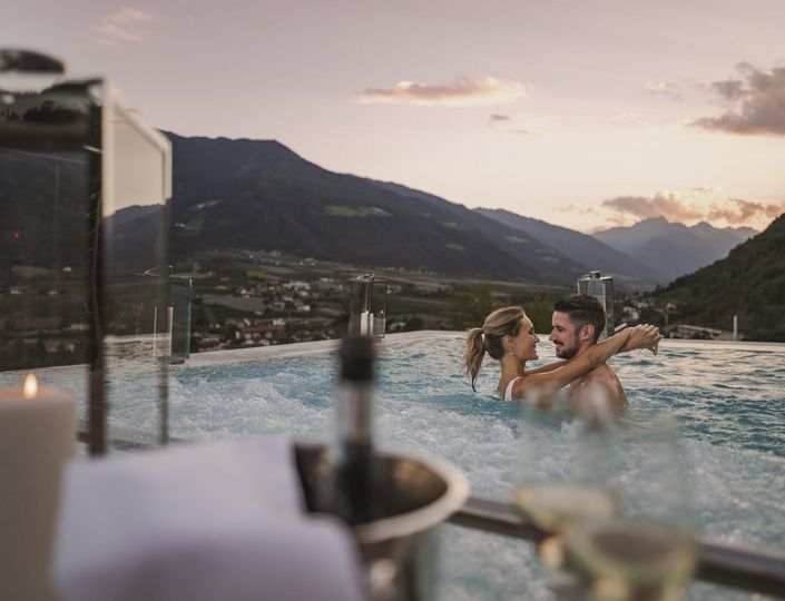 Ein Paar steht im Infinity-Pool und blickt sich vor der Bergkulisse beim Sonnenuntergang an.
