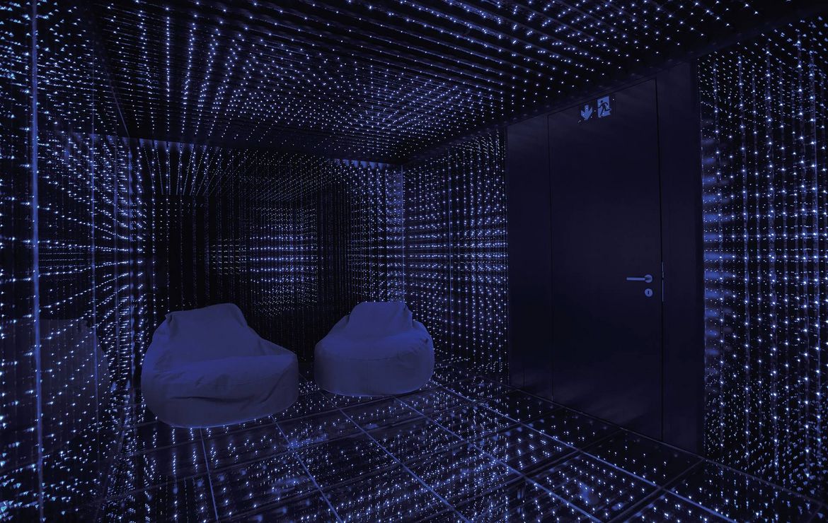 Una sala trattamento a specchi con due chaise longue e pattern di luci LED blu su pareti e pavimento.
