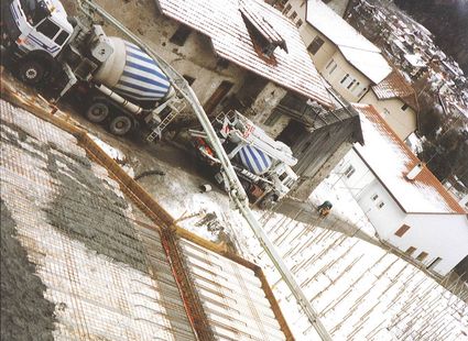 Eine schneebedeckte Baustelle mit Betonmischern und Gebäuden im Hintergrund.