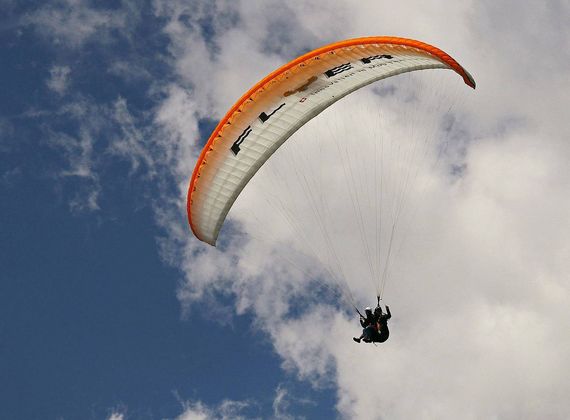 Ein Paraglider schwebt vor blauem Himmel und Wolken in großer Höhe.