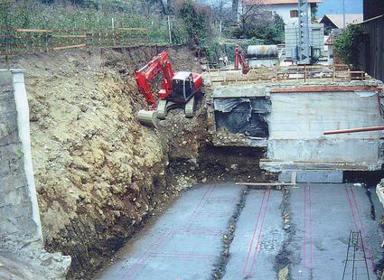 Ein Bagger arbeitet an einer großen Baugrube neben einem massiven Betonbauwerk.