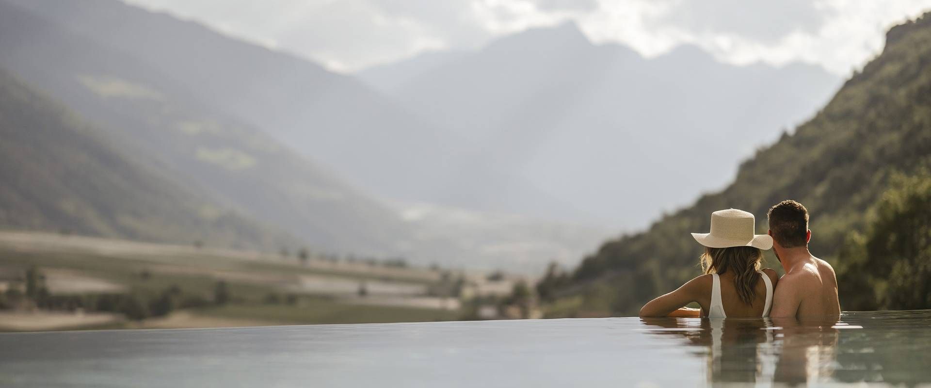 Ein Paar steht im Infinity-Pool und blickt auf die Berge im Tal.
