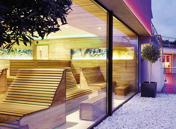 Eine moderne Sauna mit Holzliegen und Glasfront neben einem hellen Außenbereich.