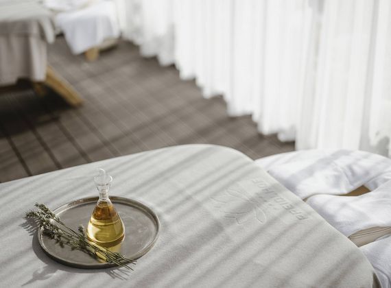 Un lettino per trattamenti è preparato con un vassoio, una bottiglia d'olio ed erbe in una sala spa luminosa.