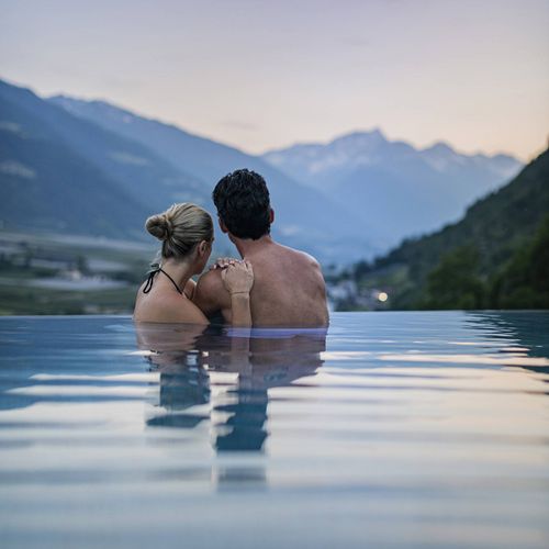 Ein Paar sitzt im Infinity-Pool und blickt in die Berge bei Abendstimmung.