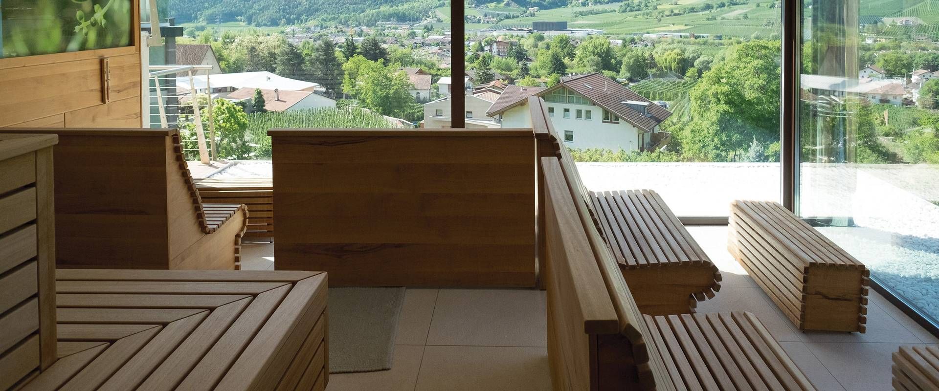 Wooden benches and a sauna lounge face large windows overlooking a green valley and houses below.
