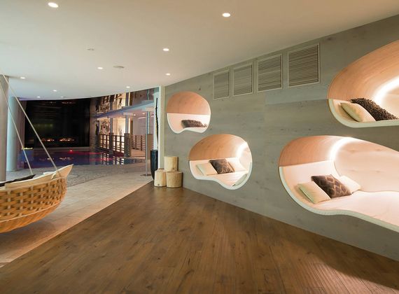 A modern sauna lounge with oval wall niches, cushions, and a hanging chair beside the pool area.
