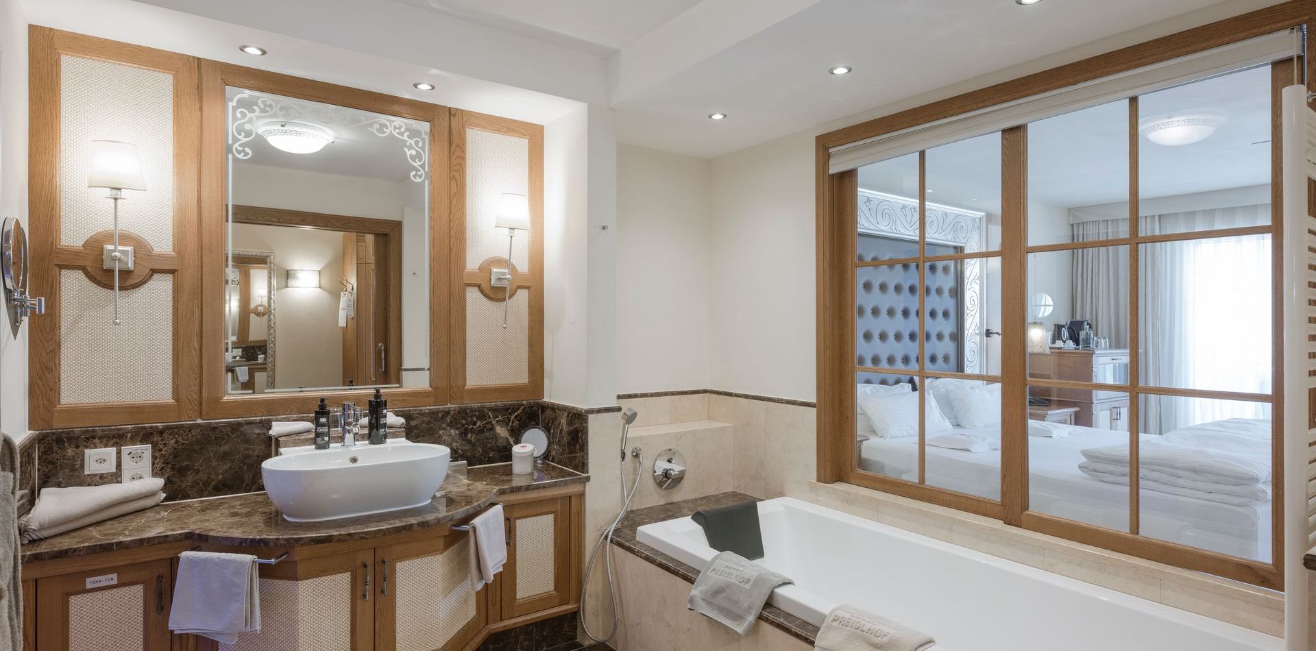 Ein helles Badezimmer der Luxury Suite Lavendel mit Doppelwaschtisch, Badewanne und Blick ins Schlafzimmer.