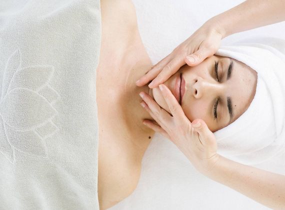 A therapist gently massages a woman's face during a spa facial treatment.