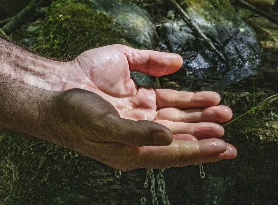 Wasser über offenen Händen im Spa-Bereich Hände halten Wasser unter einem kleinen Bach im Spa-Bereich zwischen dunklen Steinen.