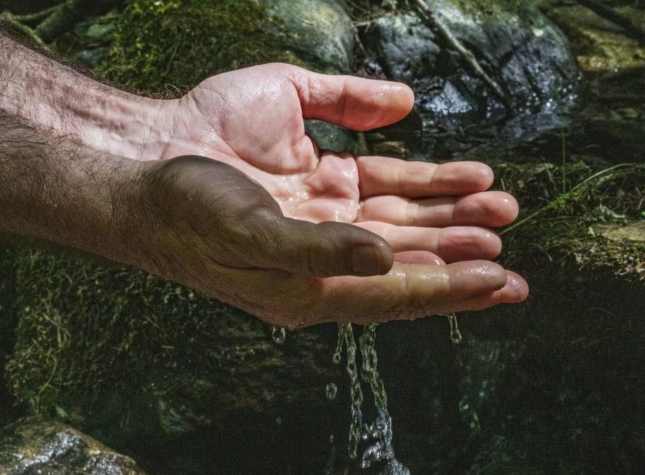 Wasser über offenen Händen im Spa-Bereich Hände halten Wasser unter einem kleinen Bach im Spa-Bereich zwischen dunklen Steinen.