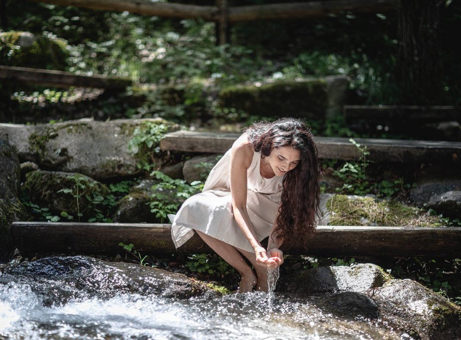 Eine Frau trinkt Wasser aus einem Fluss.