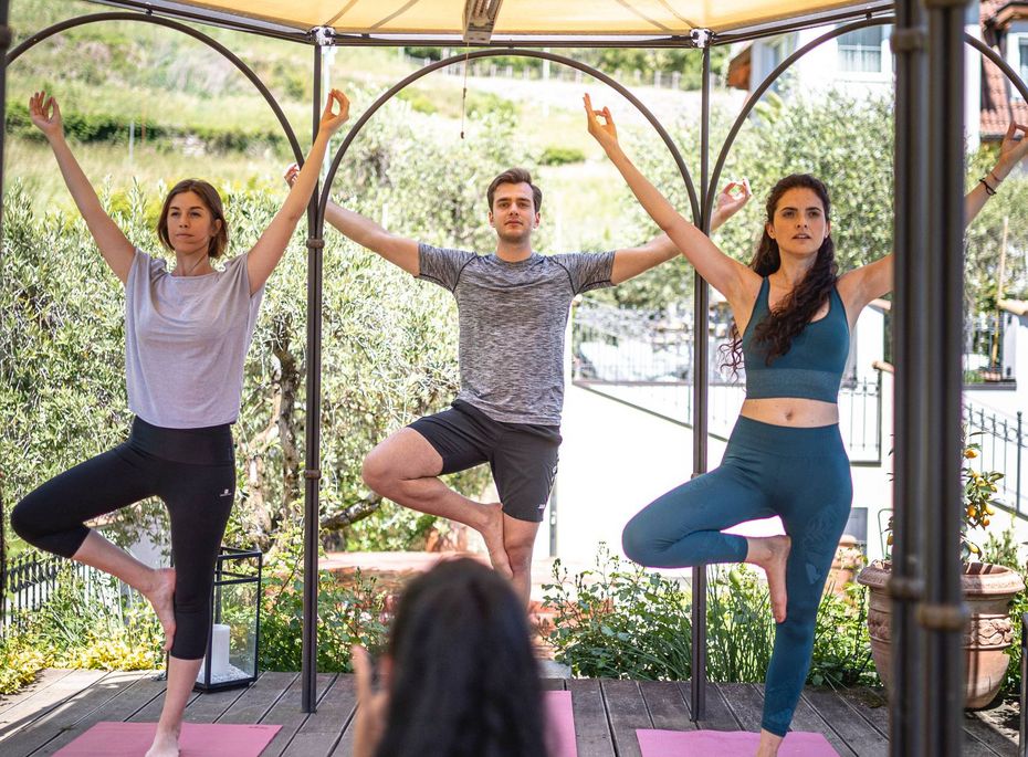Yoga im Freien im Preidlhof Wellnesshotel Drei Personen üben Yoga in einem Pavillon auf Matten, während eine Instruktorin im Vordergrund anleitet.