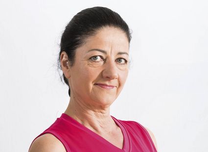 A woman in a pink top poses for a portrait against a plain light background.