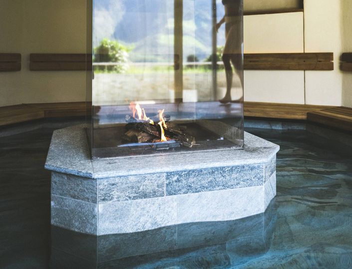 A glass-enclosed fire feature stands in the middle of an indoor spa pool.