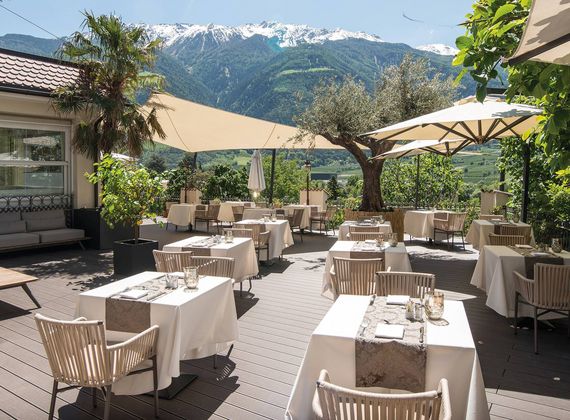 Terrazza esterna del ristorante dell'hotel con tavoli apparecchiati, ombrelloni e vista sulle montagne.