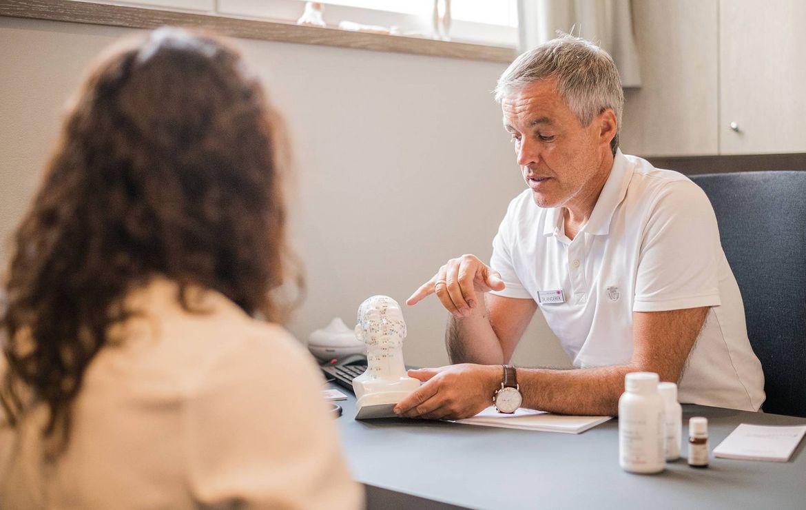 A doctor speaks with a patient across a desk in a calm consultation room.