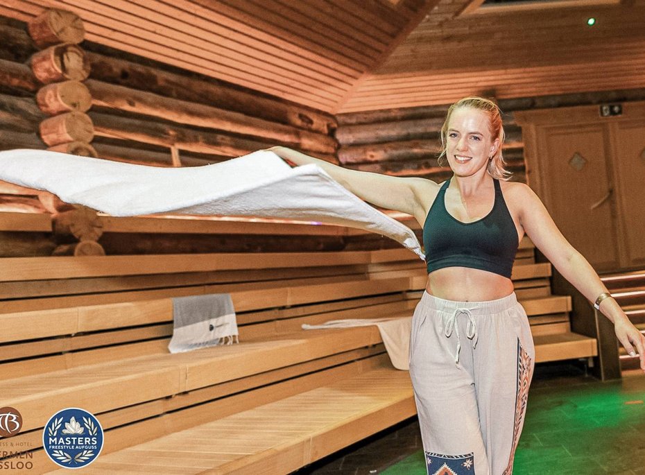 Eine Frau schwingt in einer Sauna ein Handtuch in die Luft.