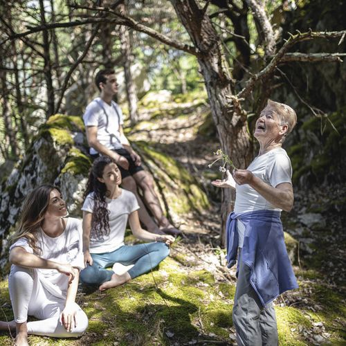 Eine kleine Wandergruppe sitzt und steht auf einem moosigen Waldweg zwischen Bäumen.