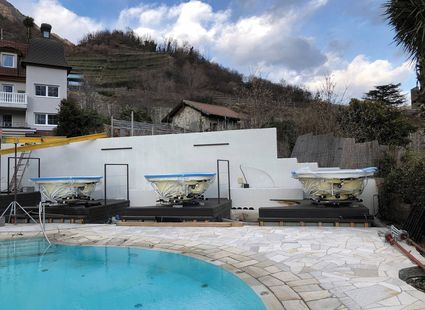 Drei Whirlpools stehen auf einer Terrasse neben dem Pool vor einer weißen Mauer und den Hängen von Naturns.