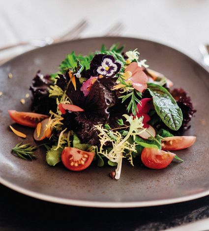 Un’insalata gourmet è servita su un piatto scuro con pomodorini e fiori eduli.